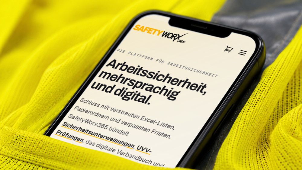 Die Startseite von SafetyWorx365 auf einem Smartphone, das in einer Warnschutzjacke steckt